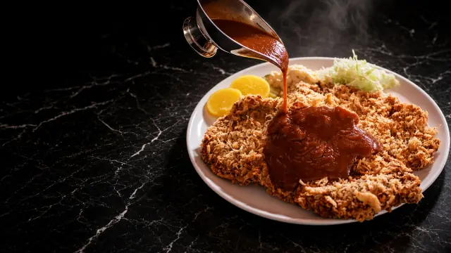 검은 대리석 위 흰 접시에 담긴 넓은 돈가스에 소스를 붓는 King Katsu 사진